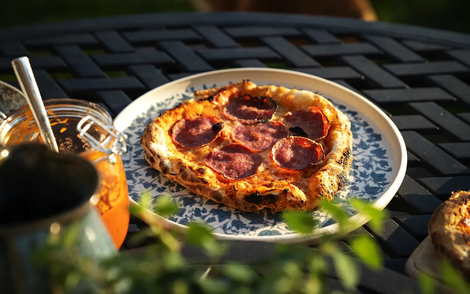 Close-up of a pizza on an outdoor table surrounded by a plant and sauces