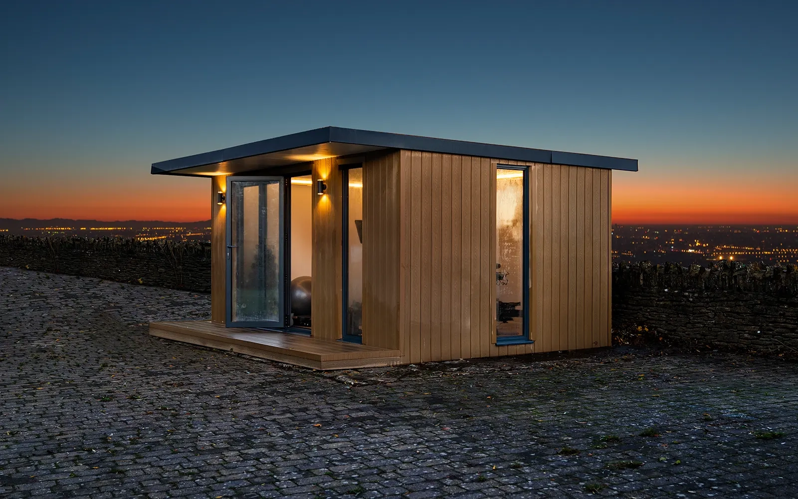 A garden room on a paved courtyard at dusk