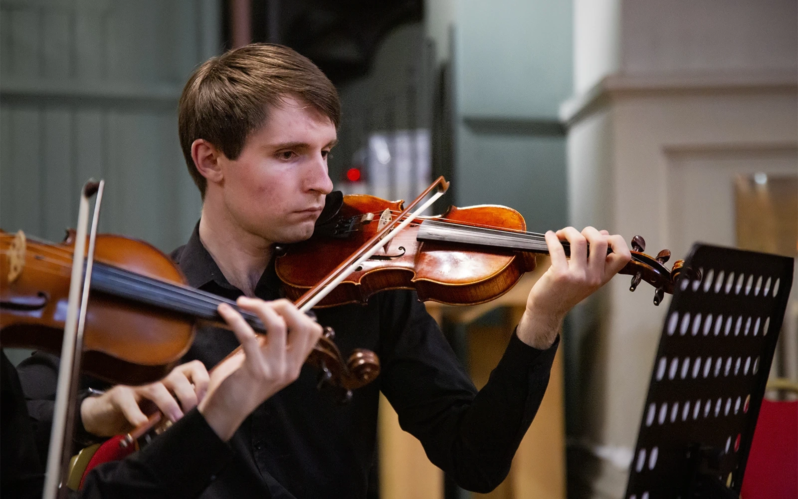 A close-up photograph of a young man playing a violin in a concert taken for use as promotional material by the Queen Mary Music Society